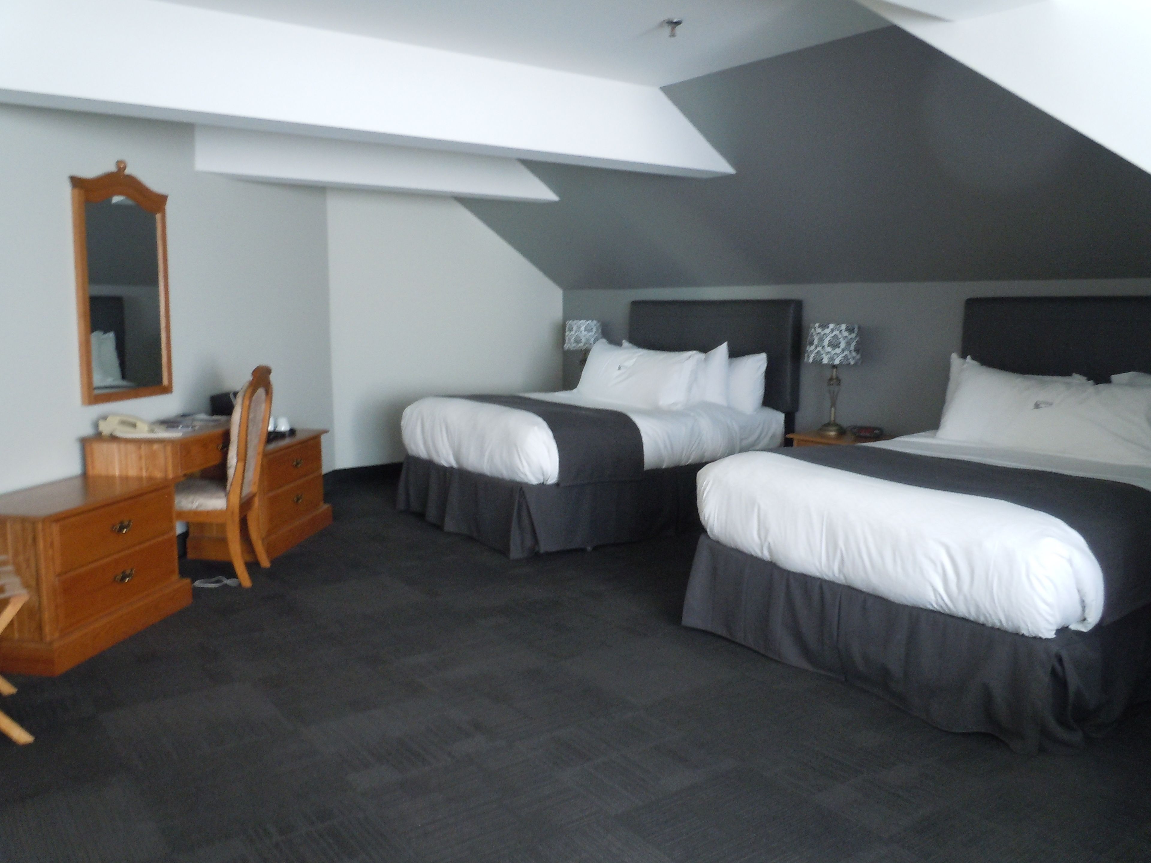 A hotel room with two beds, a desk, a chair, a dresser, and a mirror.