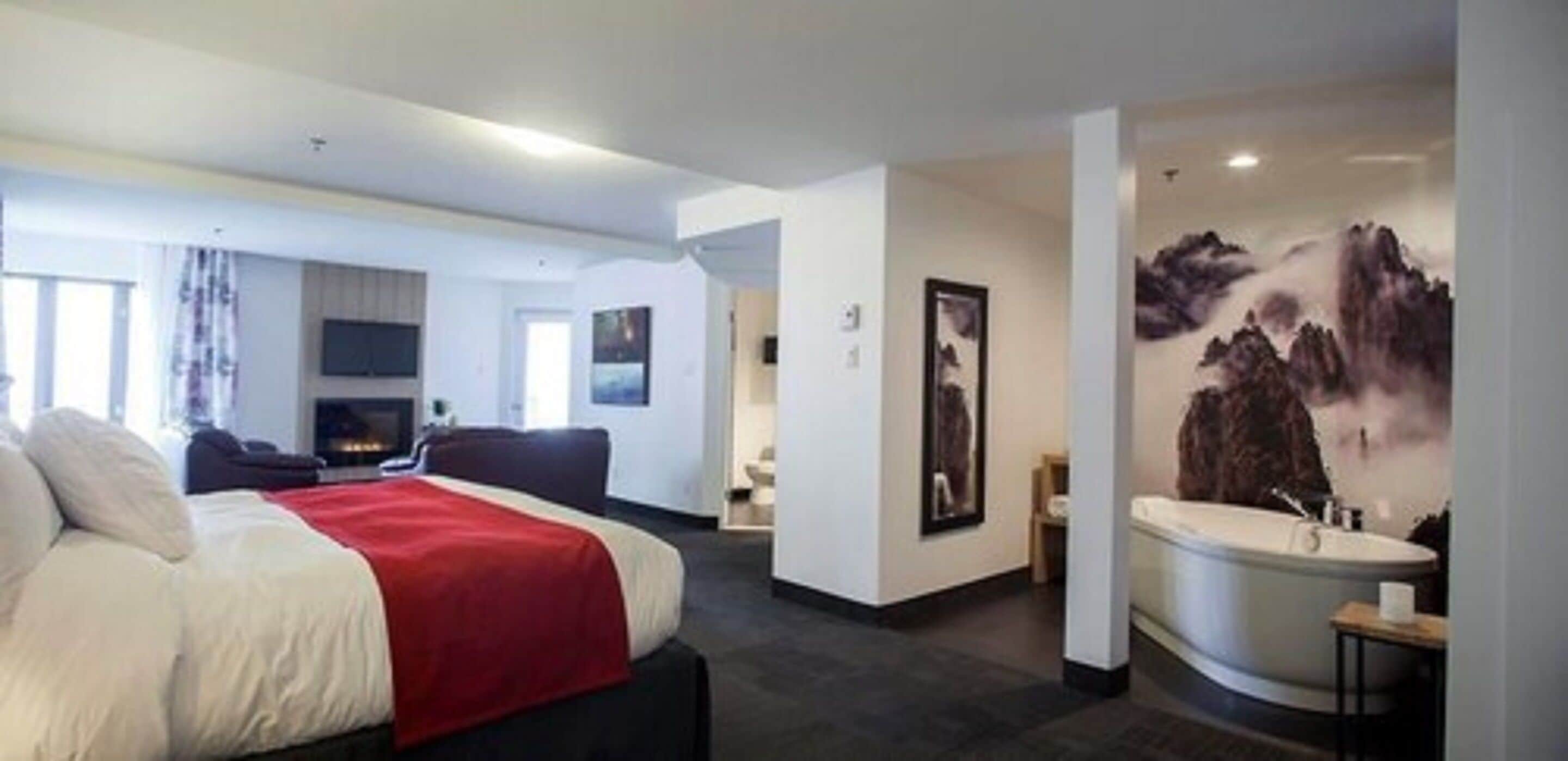 Una habitación de hotel moderna con cama, sofá, televisor, un cuadro y baño con bañera.