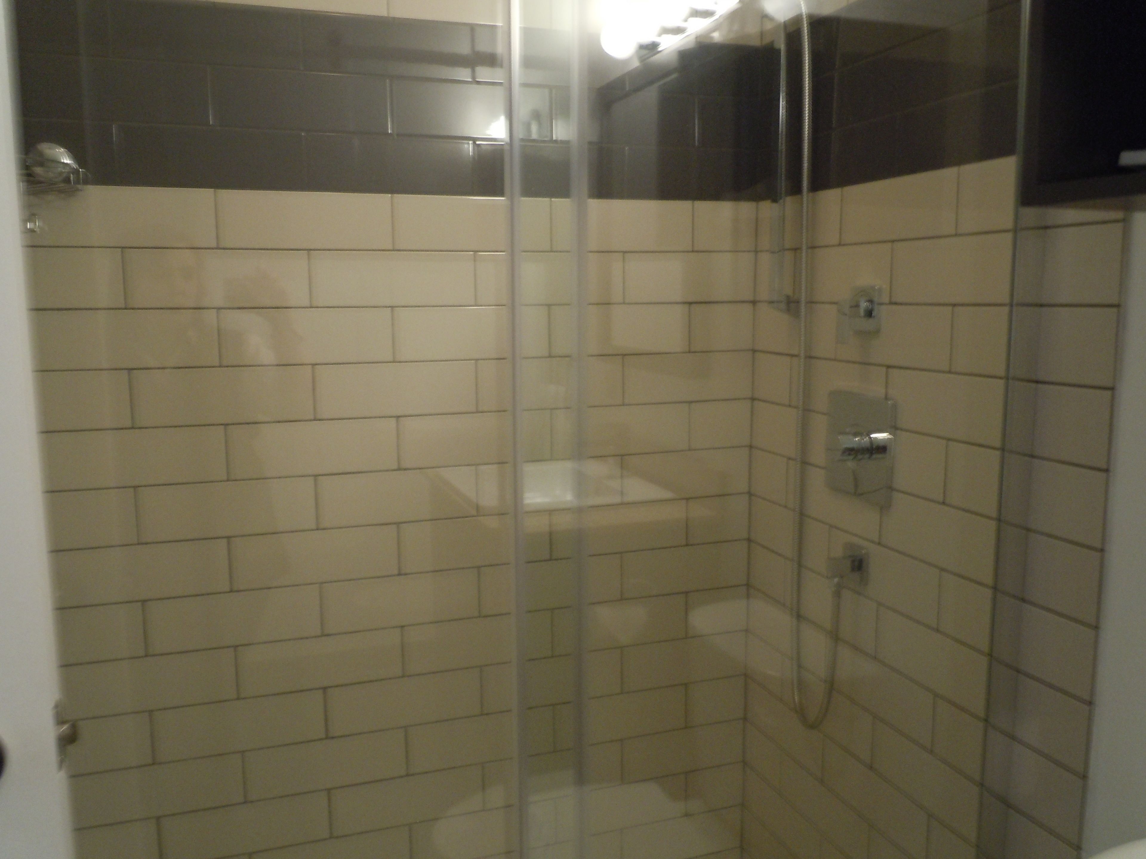 A glass-enclosed shower with beige tiles and a black-tiled upper section.