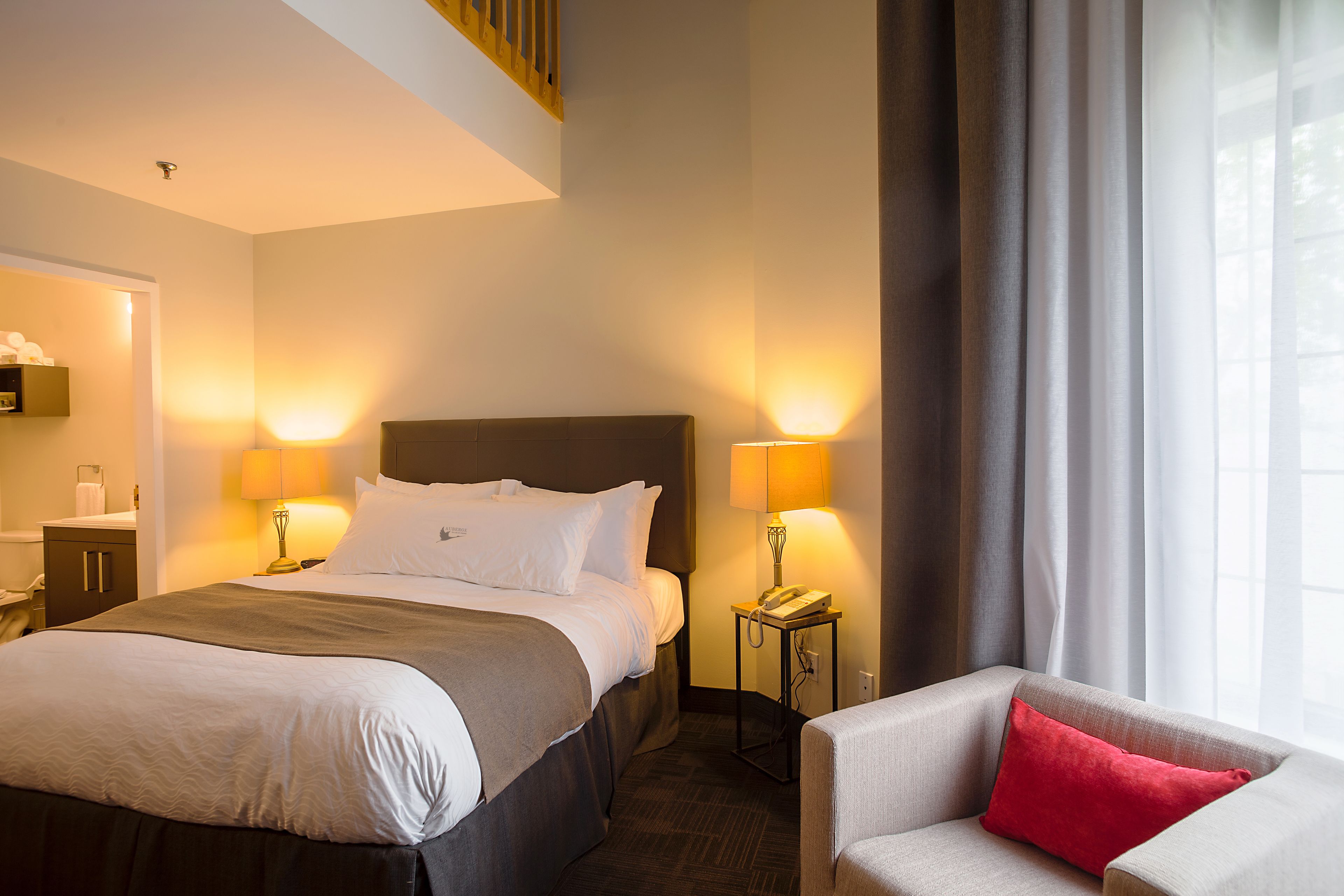 Habitación de hotel con cama, lámparas de noche, teléfono, una silla y ventana con cortinas.