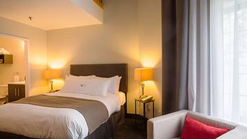 Habitación de hotel con cama, lámparas de noche, teléfono, una silla y ventana con cortinas.