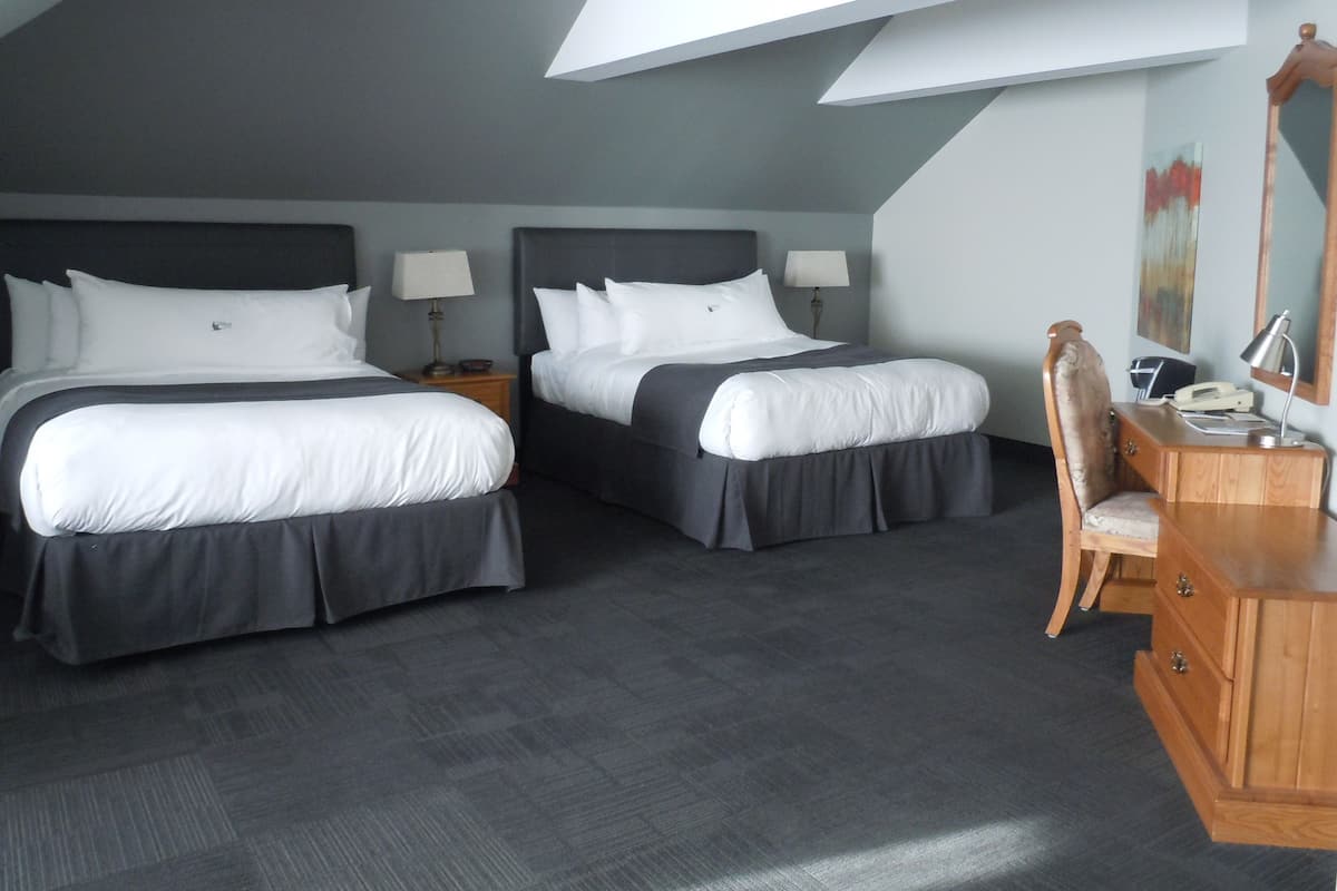 Ein Hotelzimmer mit zwei Betten, einem Schreibtisch mit Stuhl, einer Lampe und einem Bild an der Wand.