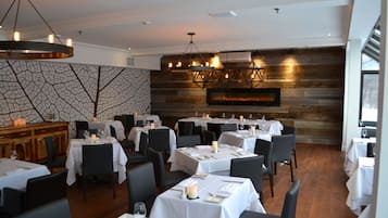 Ein Restaurant mit mehreren gedeckten Tischen, einer Holzwand mit rustikaler Maserung und einer modernen Kristallleuchtre.