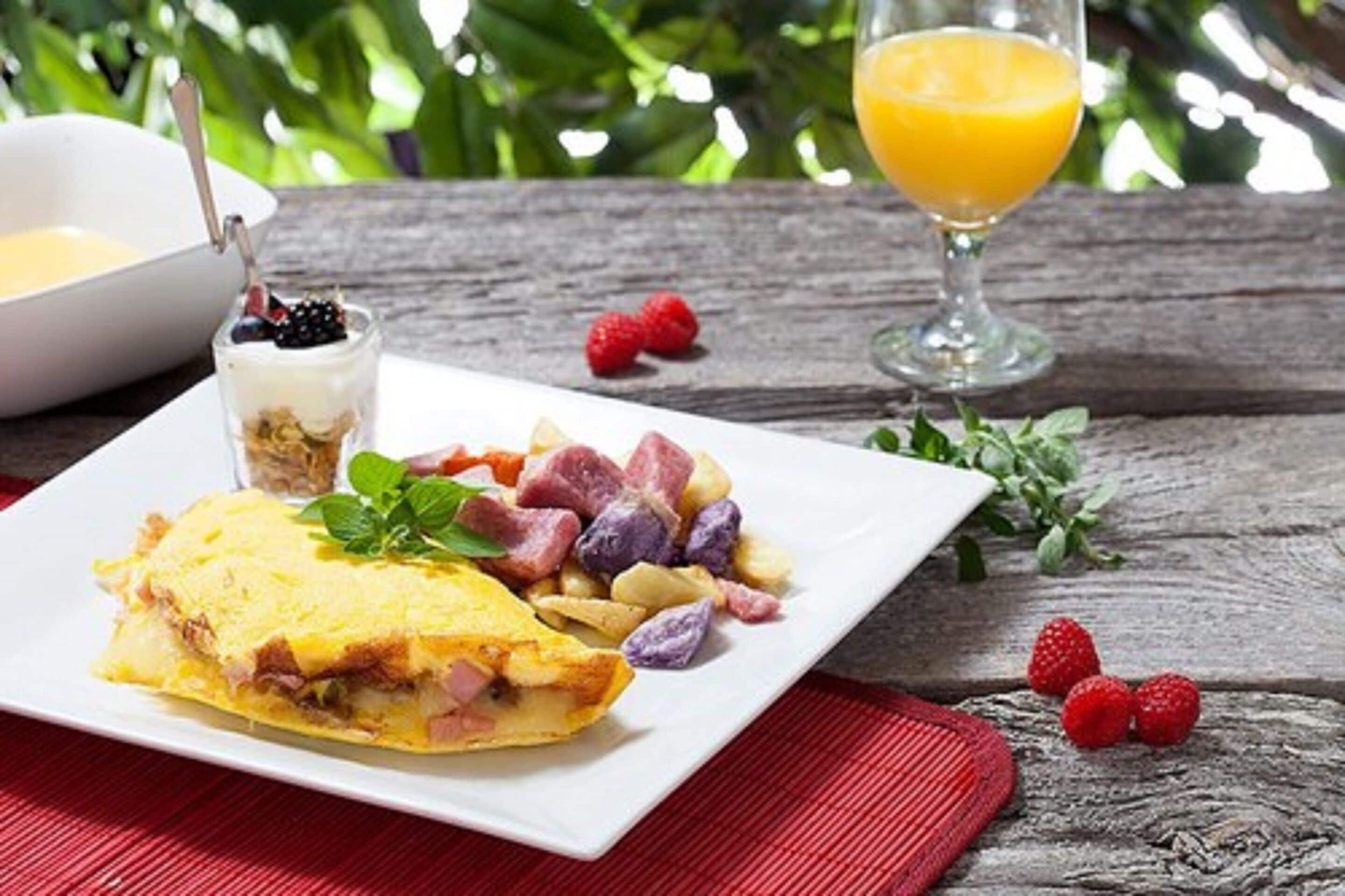 Een ontbijt bord met een omelet, fruitsalade en een glas sinaasappelsap op een houten tafel.