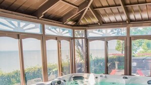 Un jacuzzi con vistas al mar, rodeado por una pérgola de madera con paneles de vidrio.