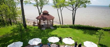 A gazebo with a view of the water, surrounded by outdoor seating with umbrellas.