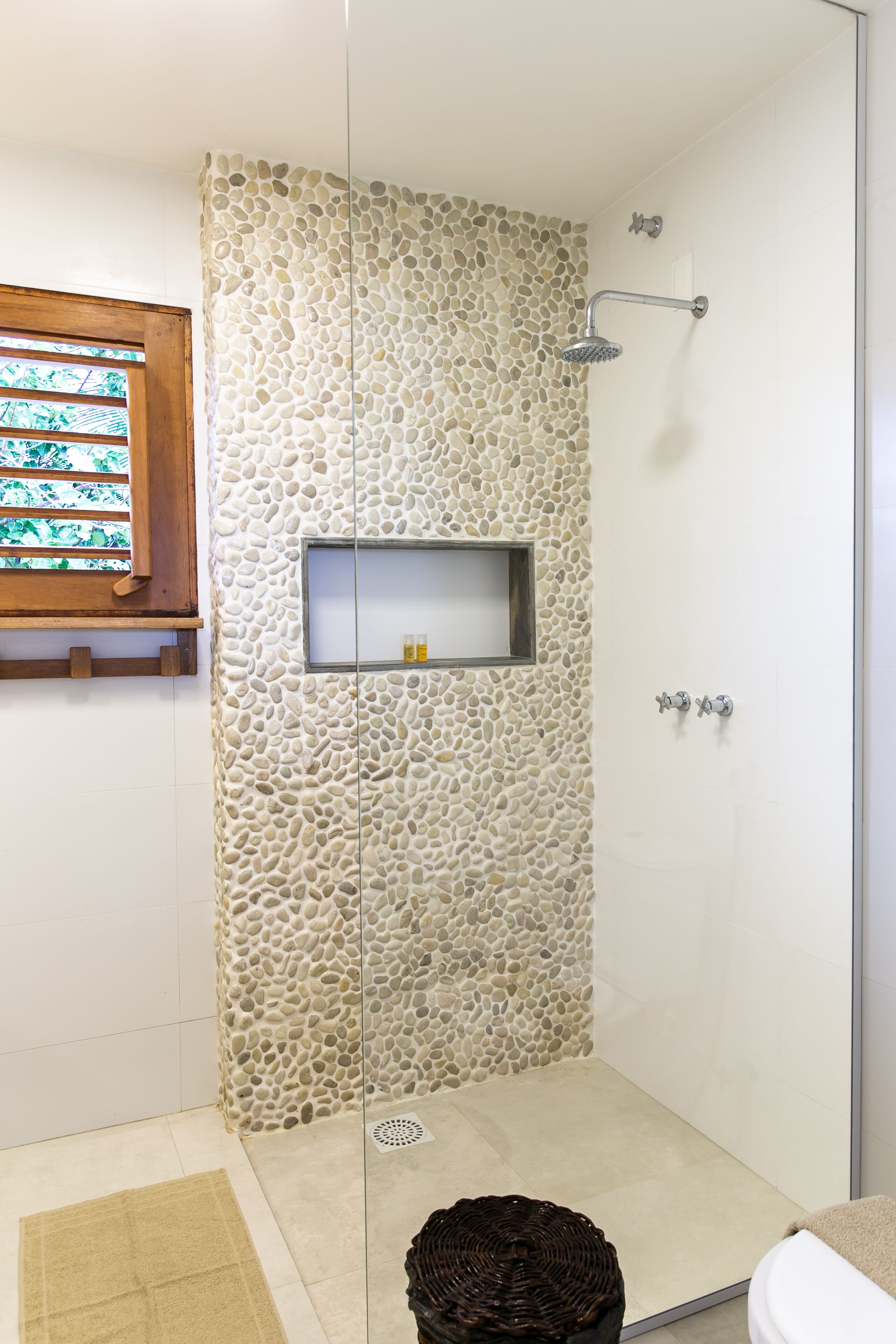 Une douche avec un mur en pierre, une étagère avec des articles de toilette et une fenêtre en bois.