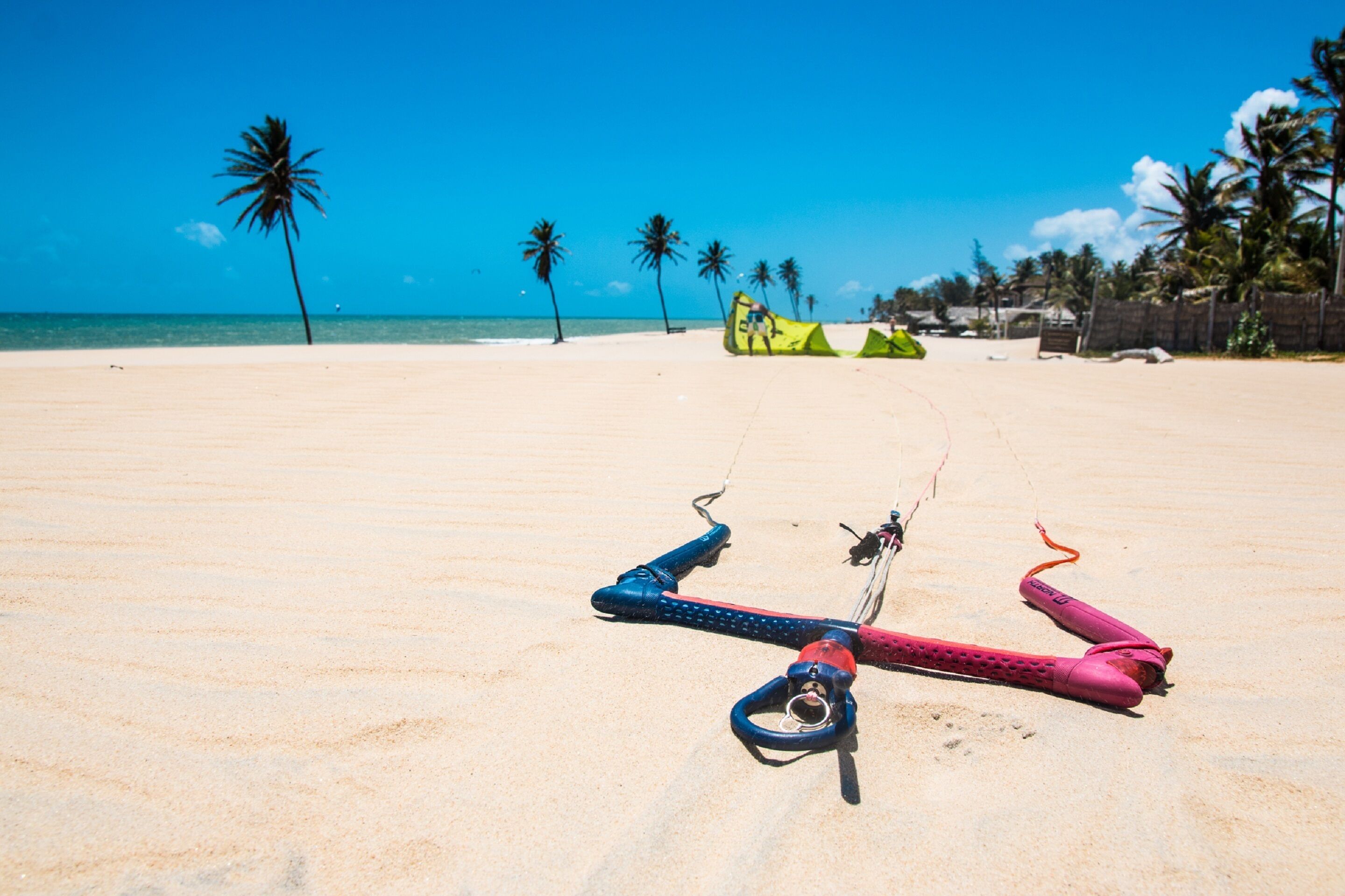 A sandy beach with a clear blue sky, palm trees, and a green tent in the background.