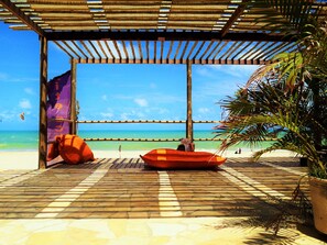 A beachside seating area with a wooden pergola, a beach umbrella, and a potted plant.