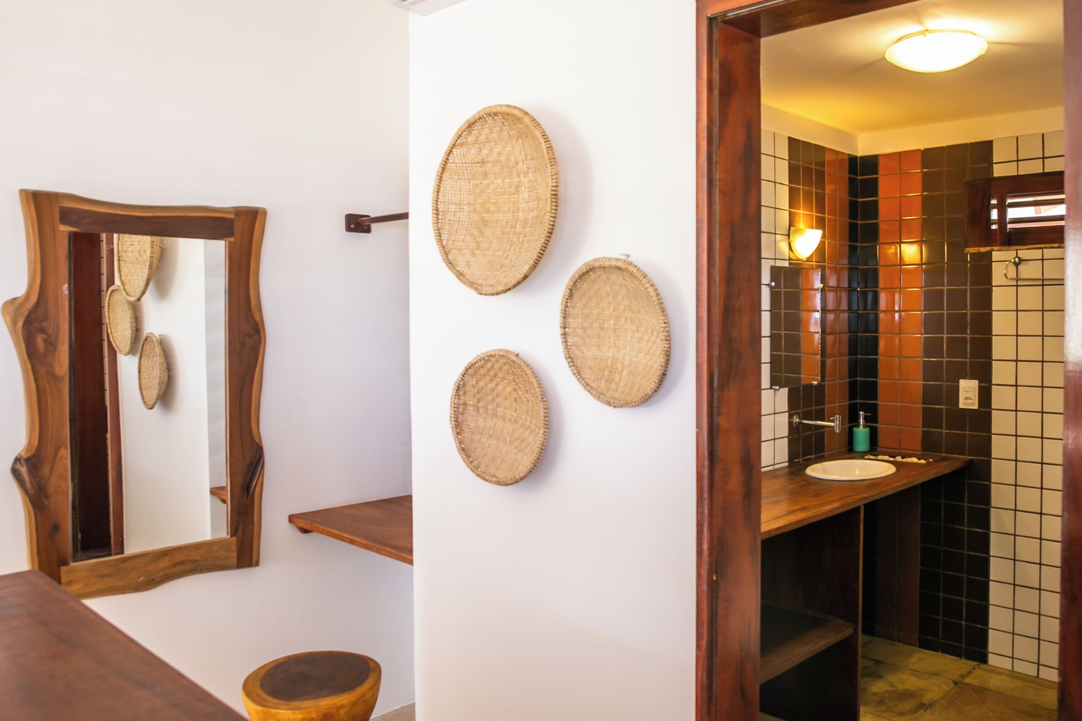 Un baño con tocador de madera, un espejo y tres adornos tejidos para la pared.