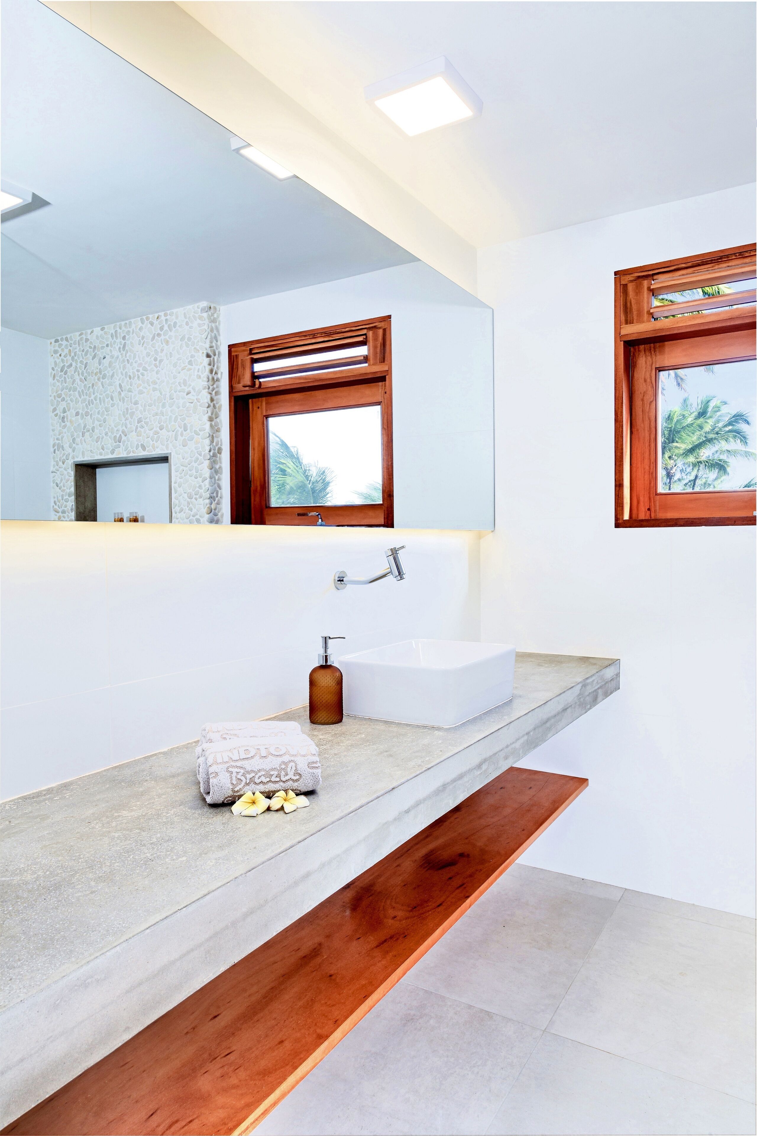 A modern bathroom with a large mirror, a white sink, and a wooden bench.