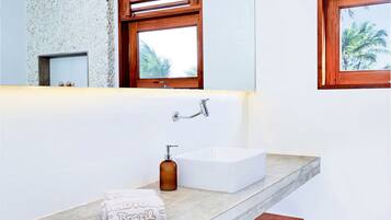 A modern bathroom with a large mirror, a white sink, and a wooden bench.