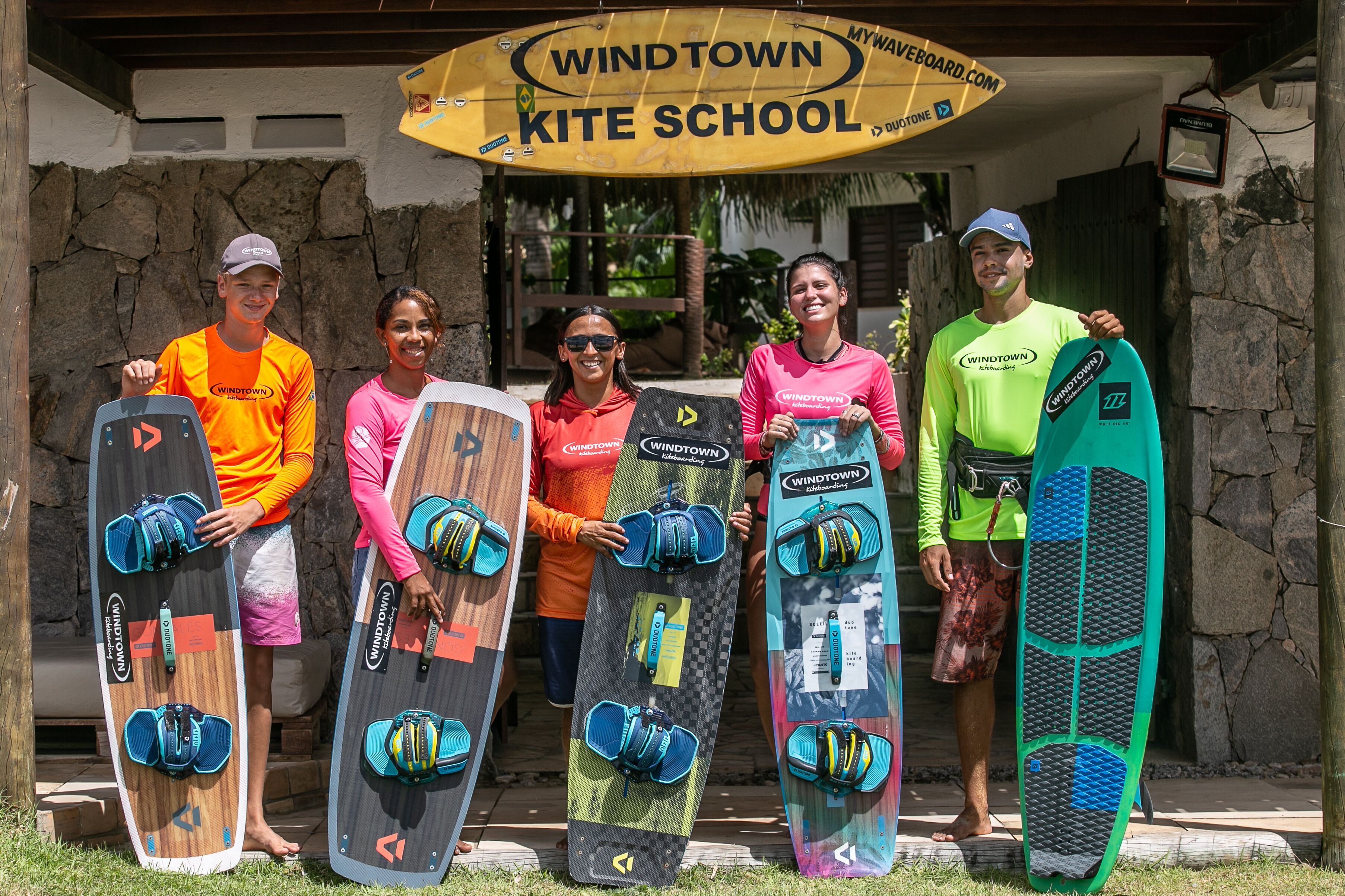 Un grupo de personas sosteniendo tablas de surf frente a un edificio con un letrero que dice 'Windtown Kite School'.