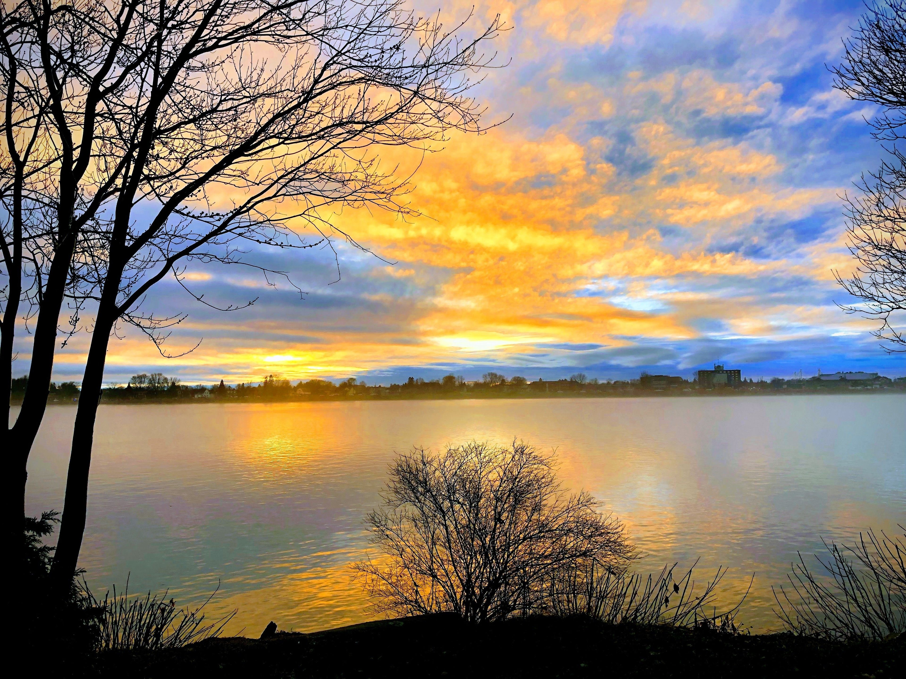 A calm lake with a sunset sky, trees, and a distant shoreline.