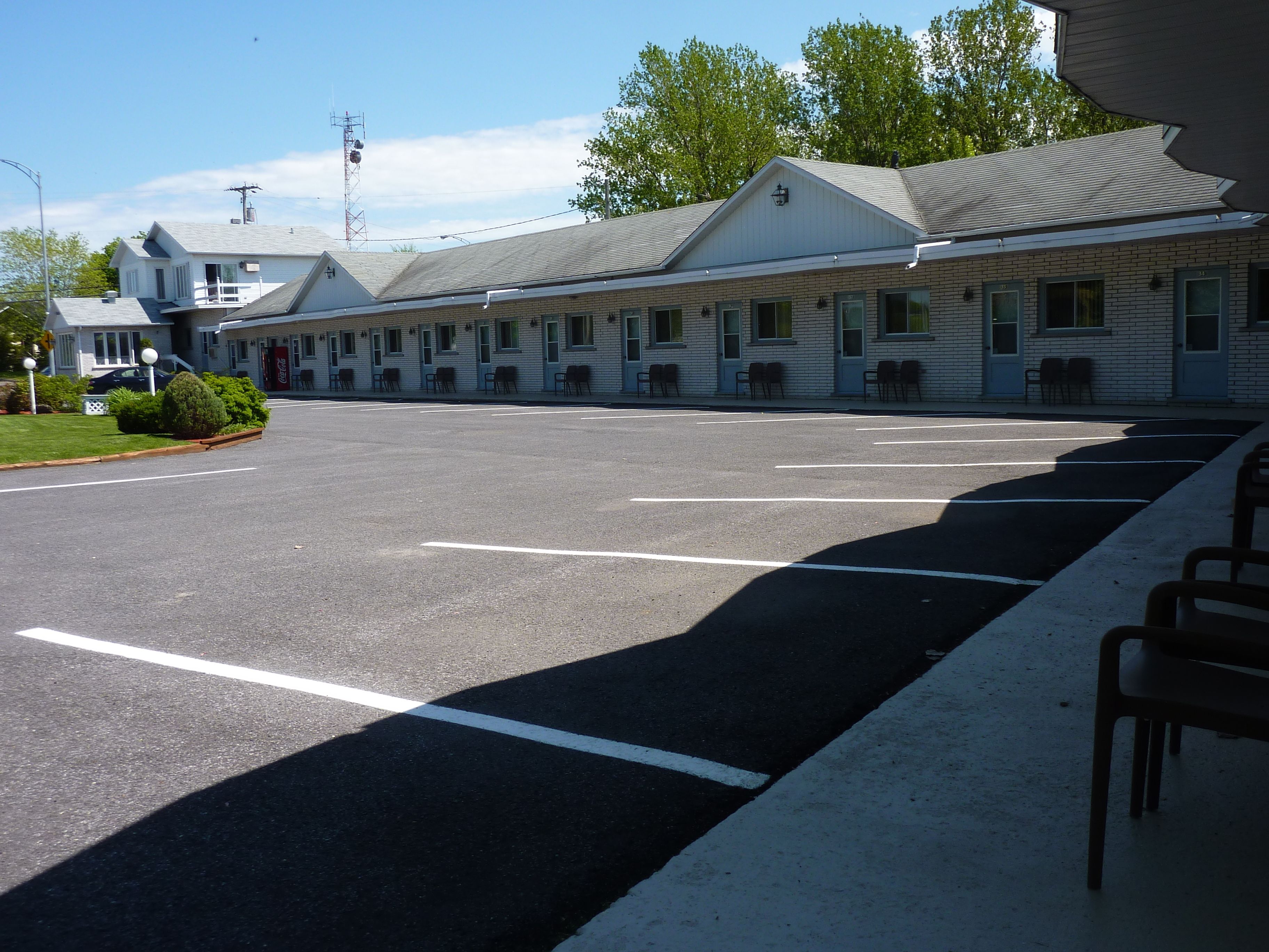 A motel with a row of rooms, a parking lot, and a building with a sloped roof.