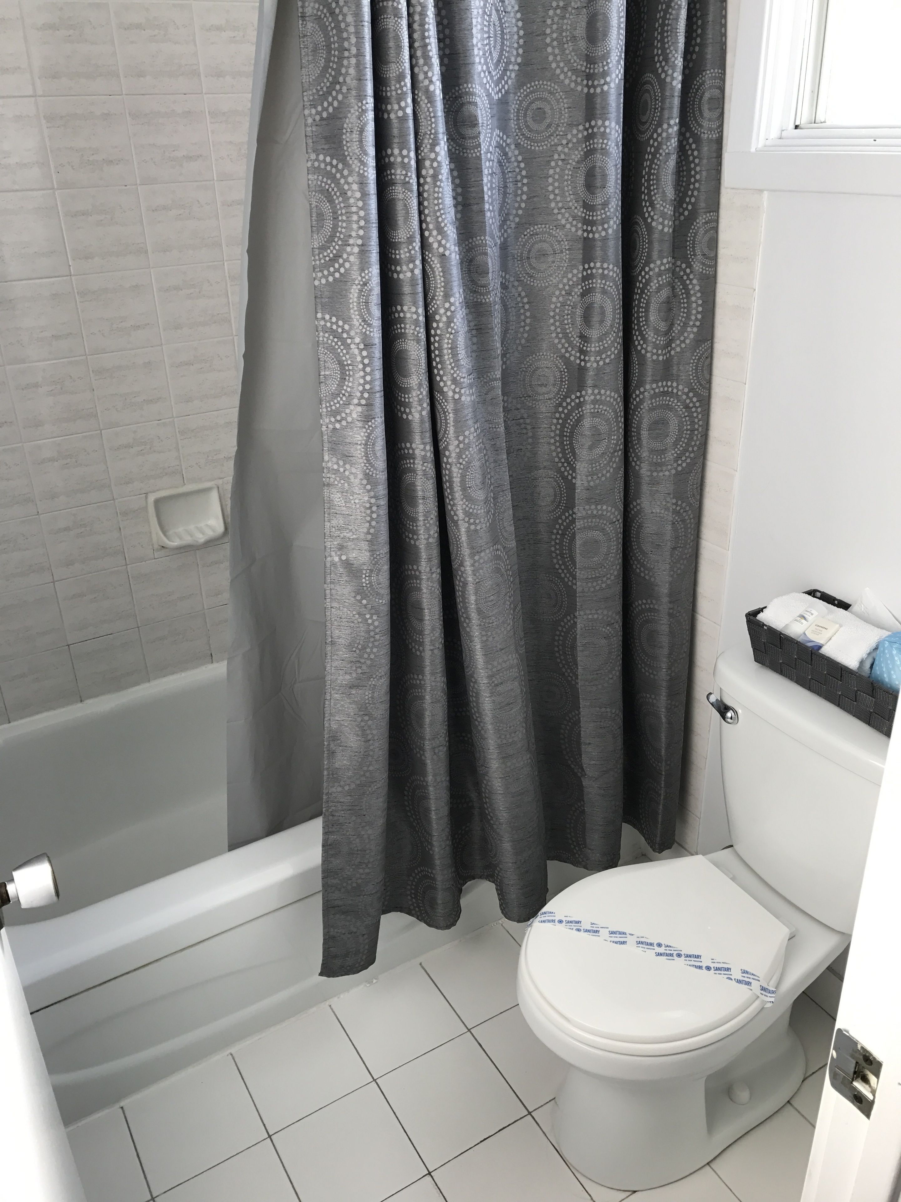 Een badkamer met een wit toilet, een badkuip en een douchegordijn met een cirkelpatroon.