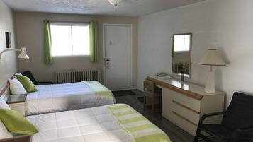 Habitación de hotel con dos camas, un escritorio, una silla, un radiador, una ventana con cortinas e iluminación en el techo.