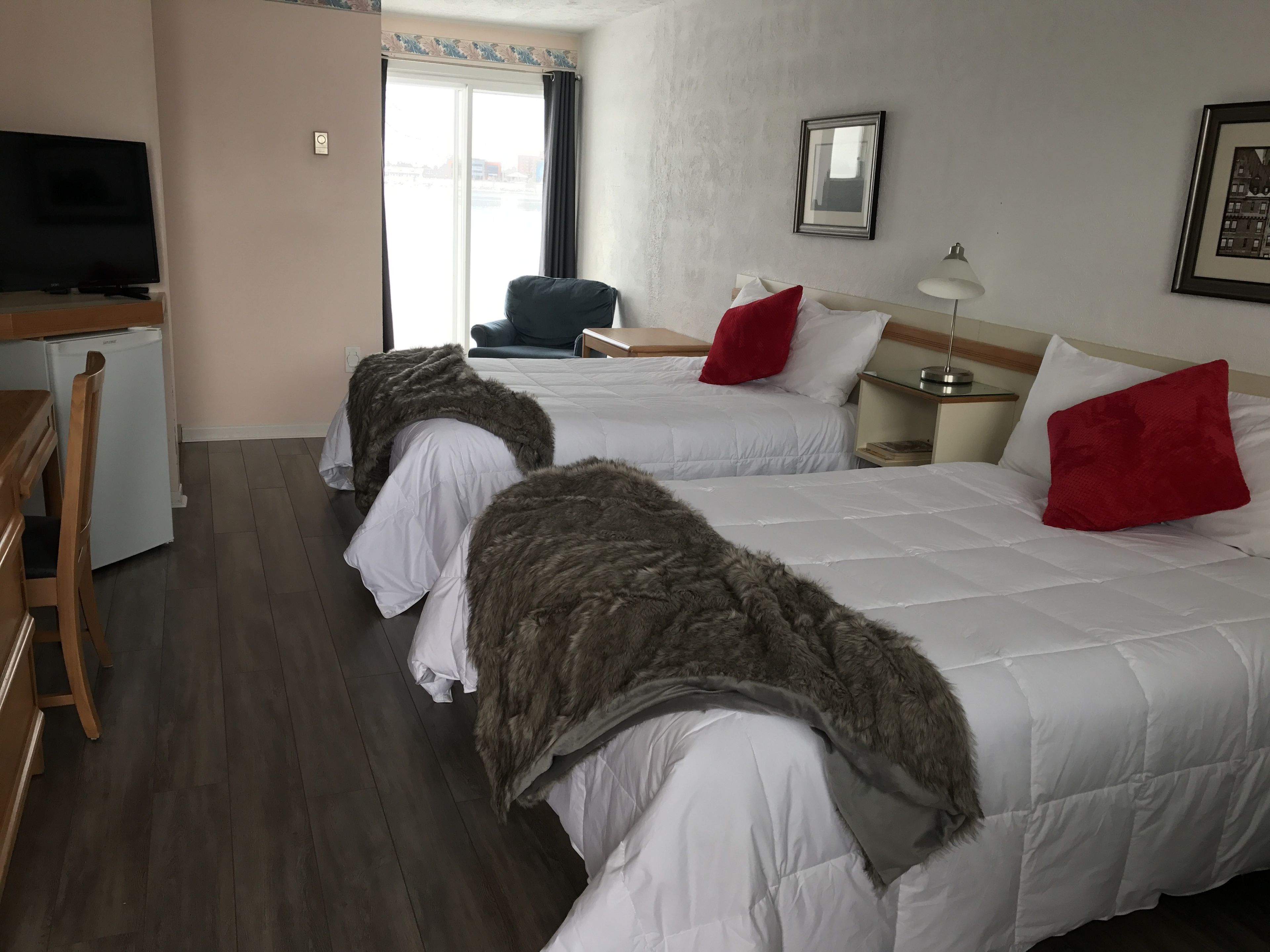 A hotel room with two beds, a desk, a television, and a window with curtains.