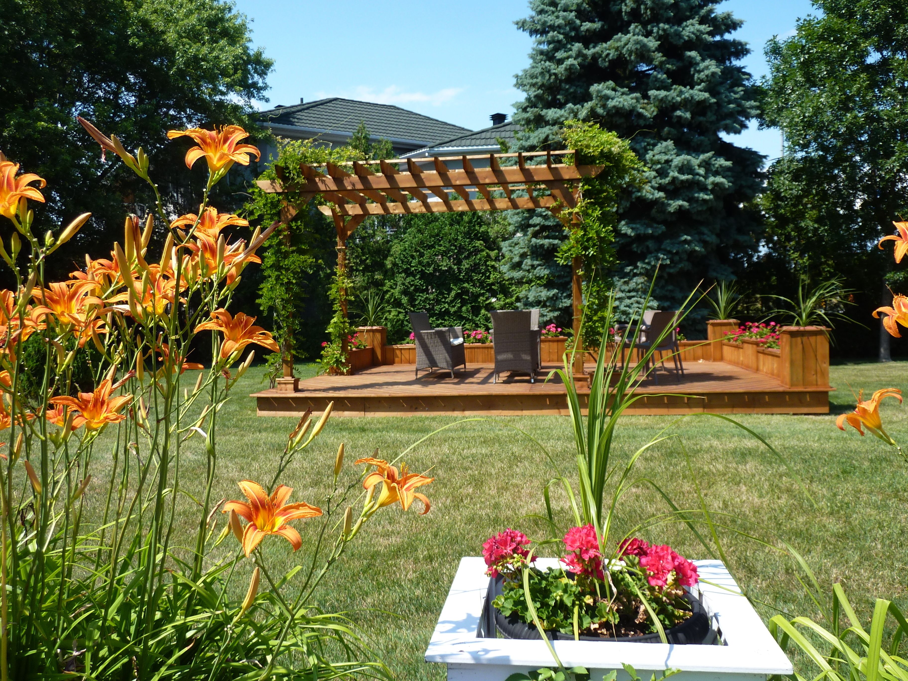 Un jardin agrémenté d’une pergola en bois, d’un espace salon extérieur et d’un parterre de fleurs.