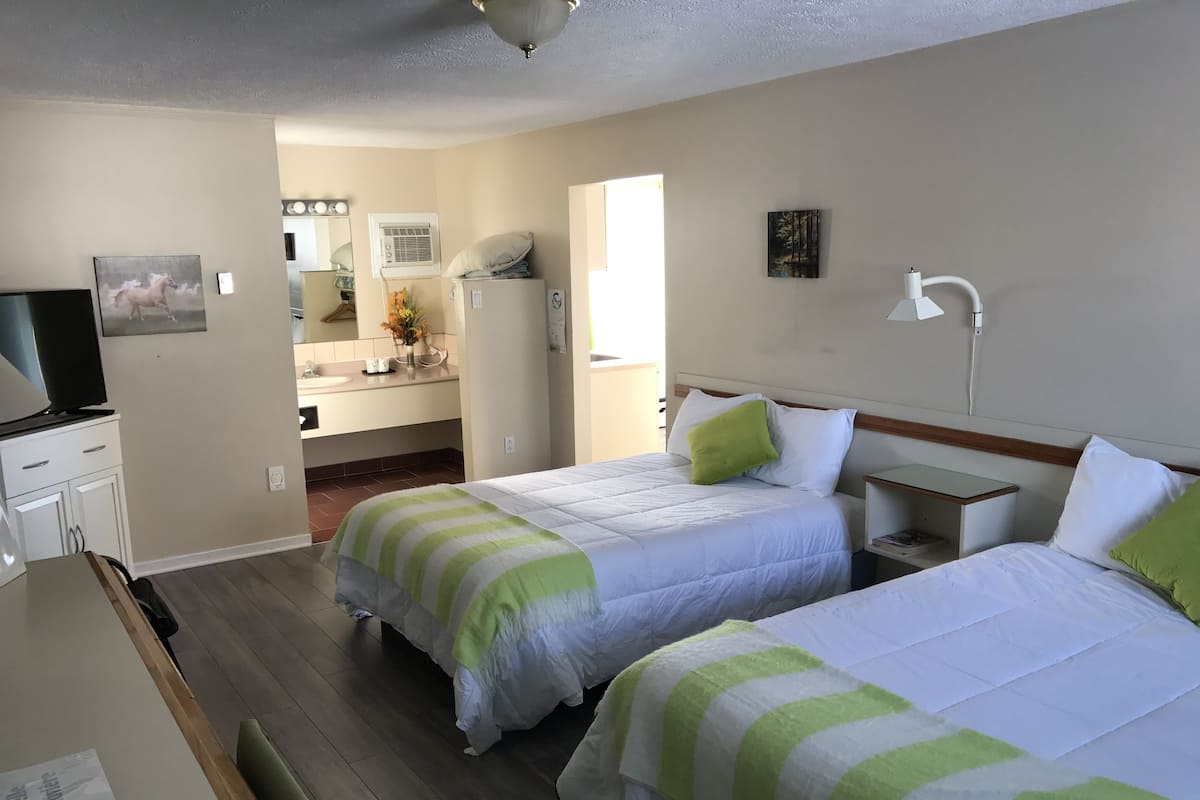 Une chambre d’hôtel avec deux lits, un bureau, une télévision et une salle de bain visible à travers une porte ouverte.
