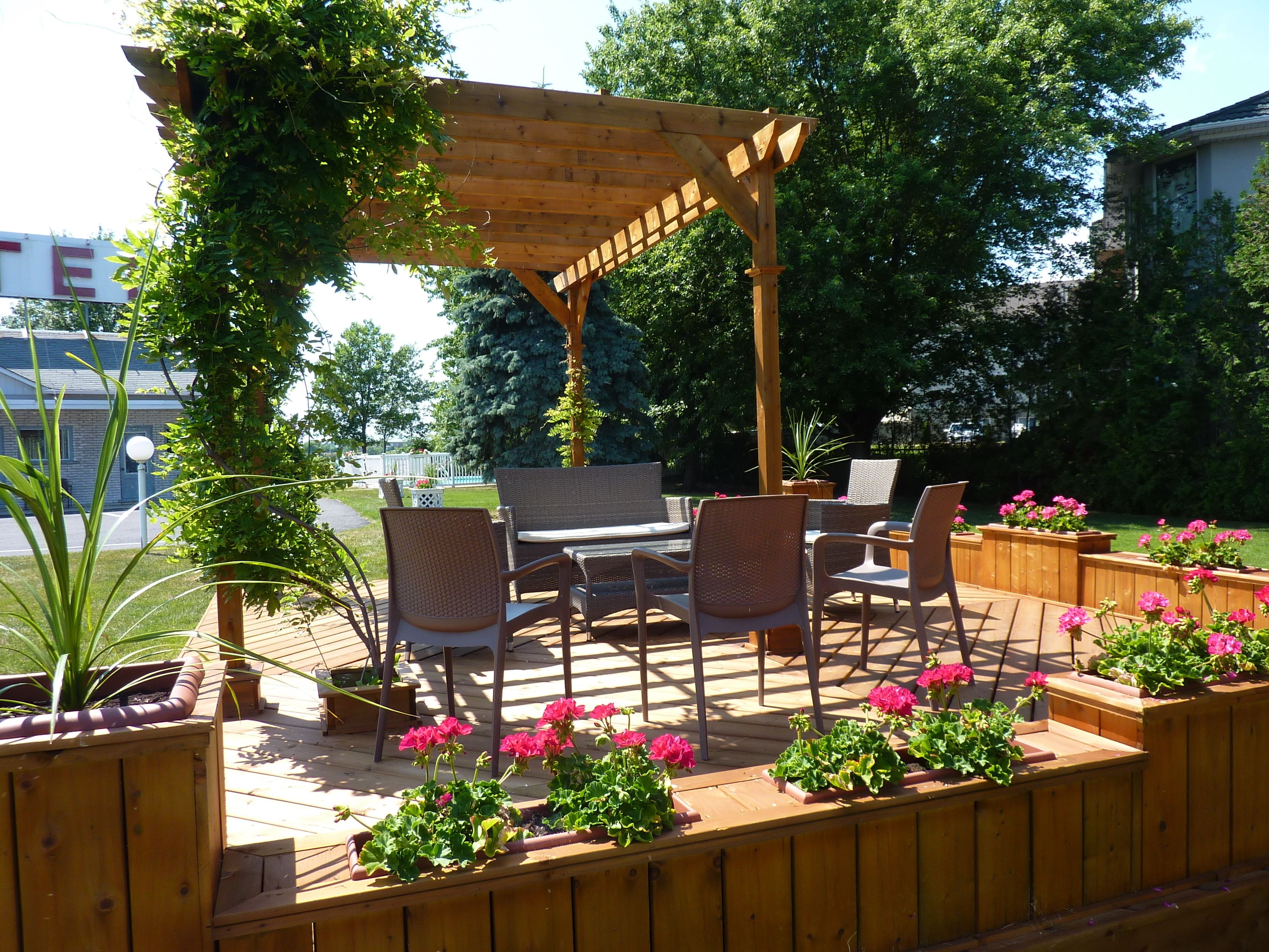Una terraza de madera con mobiliario exterior, que incluye una mesa y sillas, rodeada de macetas con flores.