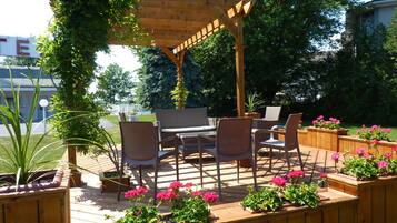 Una terraza de madera con mobiliario exterior, que incluye una mesa y sillas, rodeada de macetas con flores.