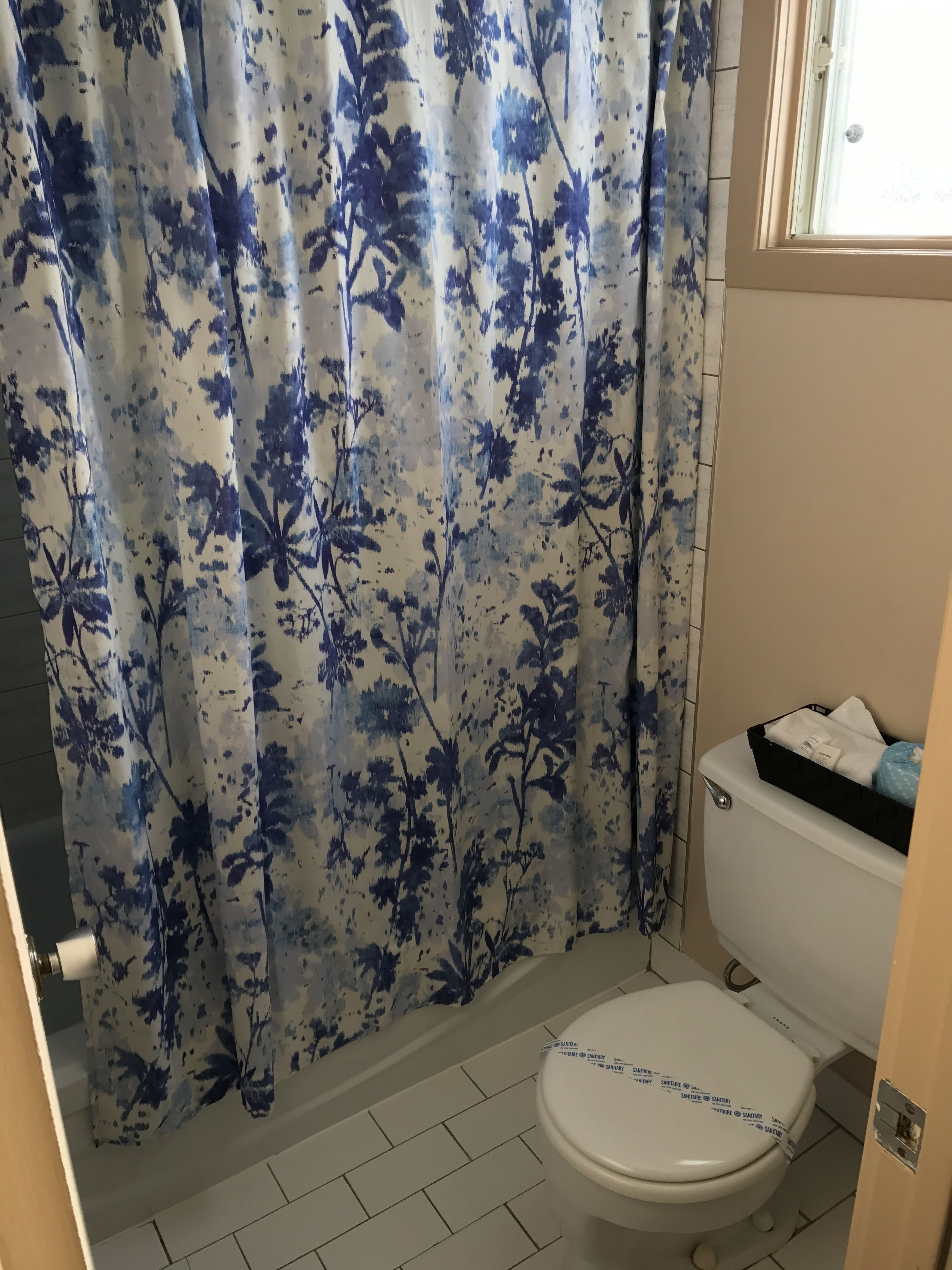 A bathroom with a toilet, a shower curtain with a floral pattern, and a small shelf with toiletries.