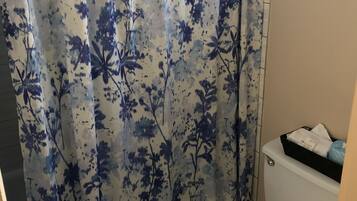 A bathroom with a toilet, a shower curtain with a floral pattern, and a small shelf with toiletries.