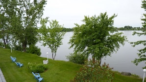 Une vue sur le lac, avec une zone herbeuse, plusieurs chaises bleues et des arbres.
