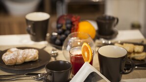 Een ontbijttafel met een bord gebak, een glas sap met een schijf sinaasappel en twee koffiemokken.