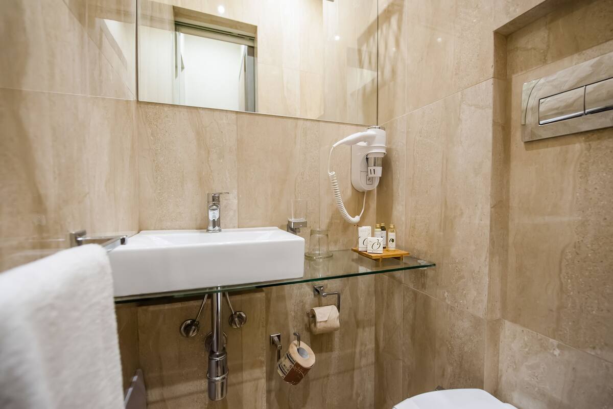 A modern bathroom with a glass shelf, a white sink, a handheld hair dryer, and a towel rack.