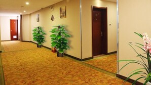 A hotel hallway with carpeted floors, potted plants, and a wooden door at the end. - GreenTree Inn Yulin Jincheng Commercial Building Shell Hotel (Yulin)