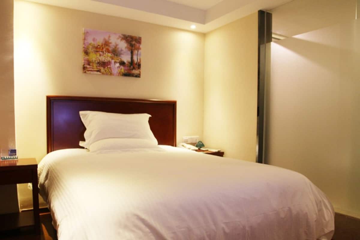 A hotel room with a large bed, a nightstand, a painting on the wall, and a window.