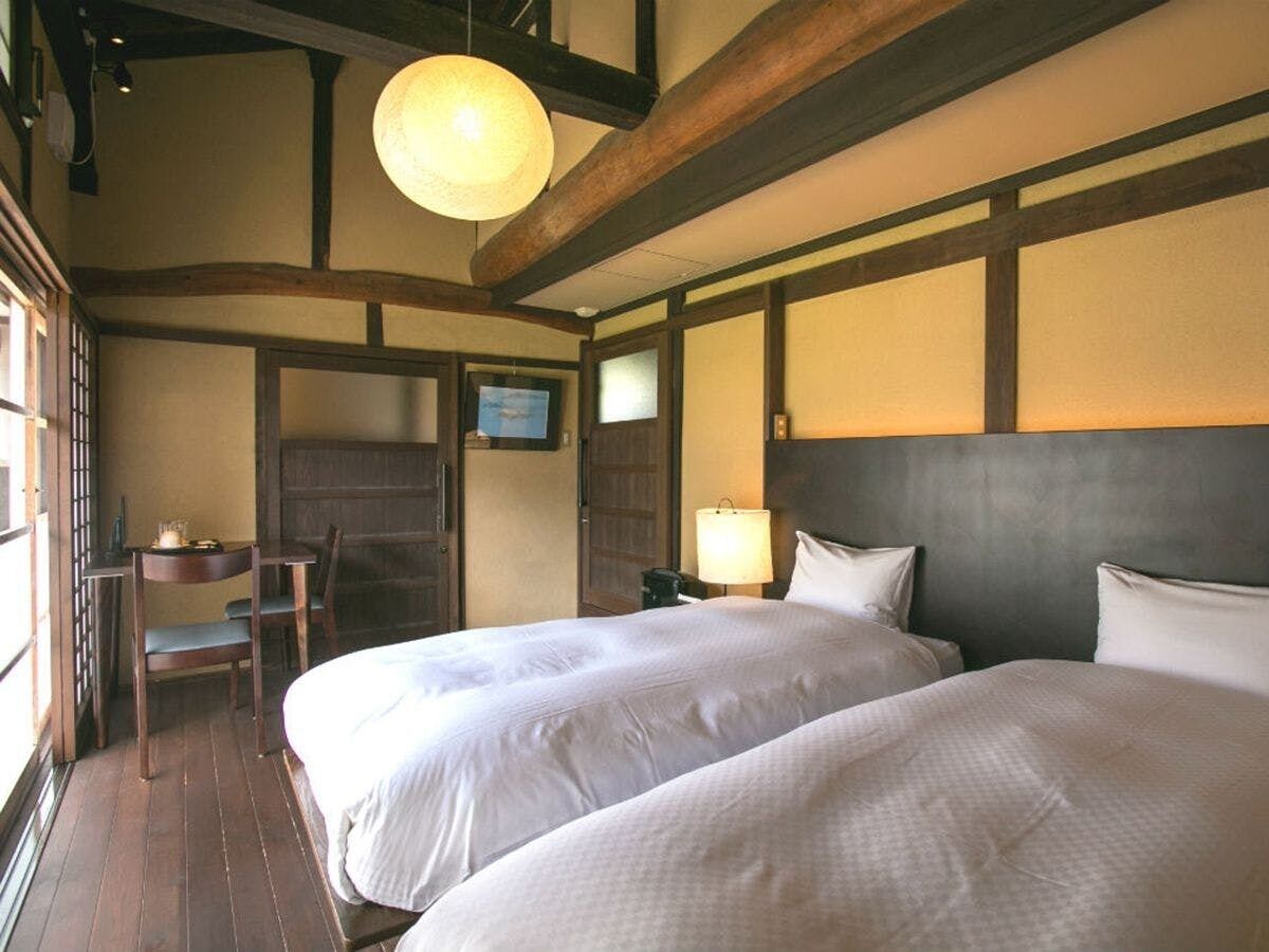 A hotel room with two beds, a desk, a chair, a television, and a lamp.