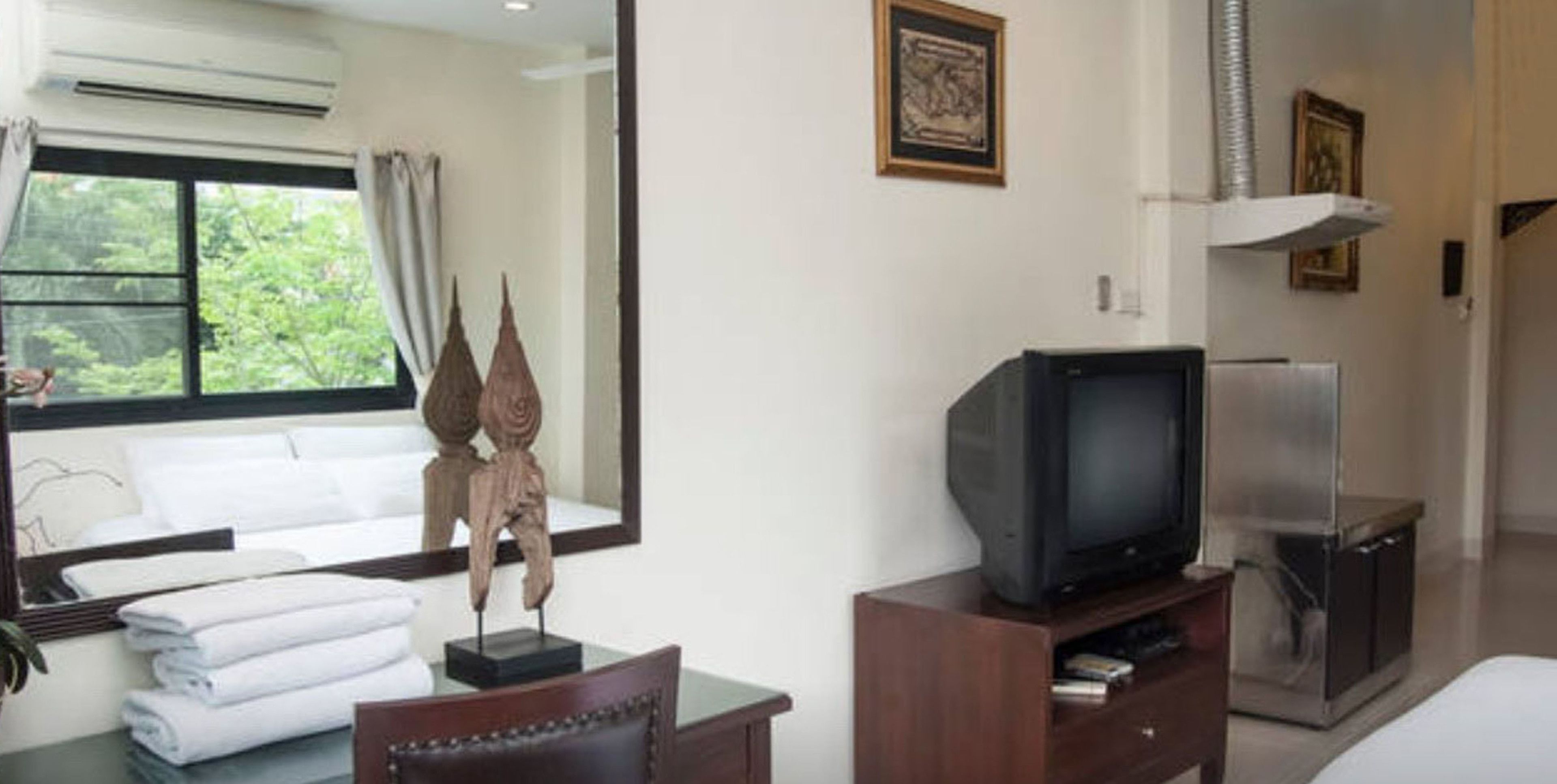 A hotel room with a bed, a television on a wooden stand, a refrigerator, and a window with curtains.