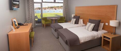 Quarto de hotel com duas camas, uma escrivaninha, uma cadeira, uma TV e vista para um estádio.