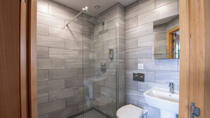 Un baño moderno con cabina de ducha de vidrio, un inodoro blanco y un lavabo con espejo superior.