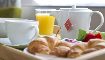 Un plateau de petit-déjeuner avec des croissants, une théière, une tasse et un verre de jus d’orange.