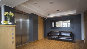 Un hall con un mostrador de recepción de madera, dos ascensores, un sofá de cuero negro y un espejo en la pared.