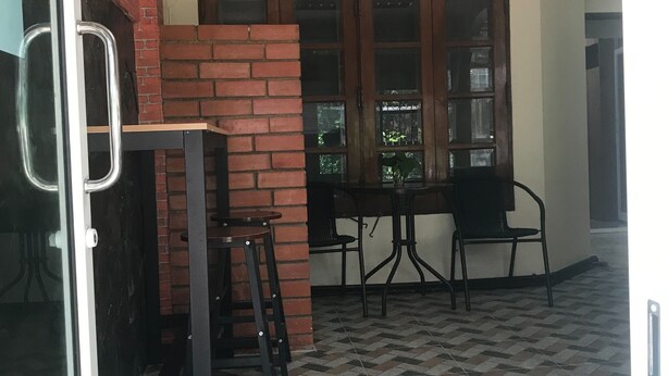 A room with a tiled floor, a brick wall, a wooden door, and a table with chairs. - Orchid House (Bangkok)