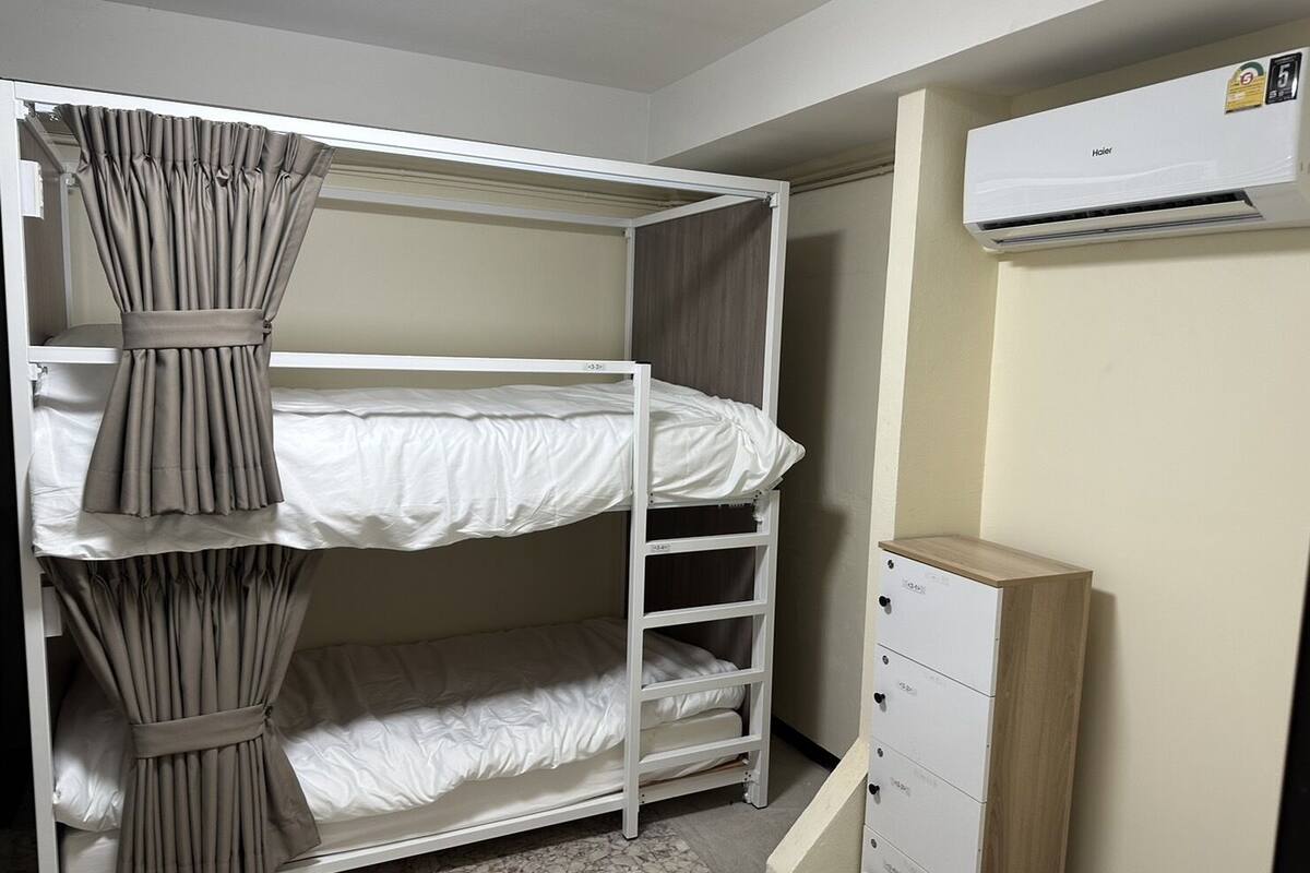 A bunk bed with curtains, a white wardrobe, and an air conditioning unit.