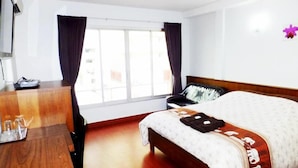 Una habitación de hotel con cama, cómoda de madera, escritorio y ventana con cortinas.