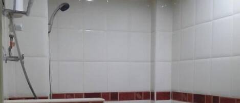 Ein kleines Badezimmer mit Fliesen, einer Dusche, einer Toilette und einem Handtuchhalter.