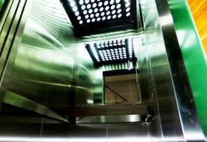 A metallic elevator interior with reflective surfaces and a green wall. - Orchid Inn (Bangkok)