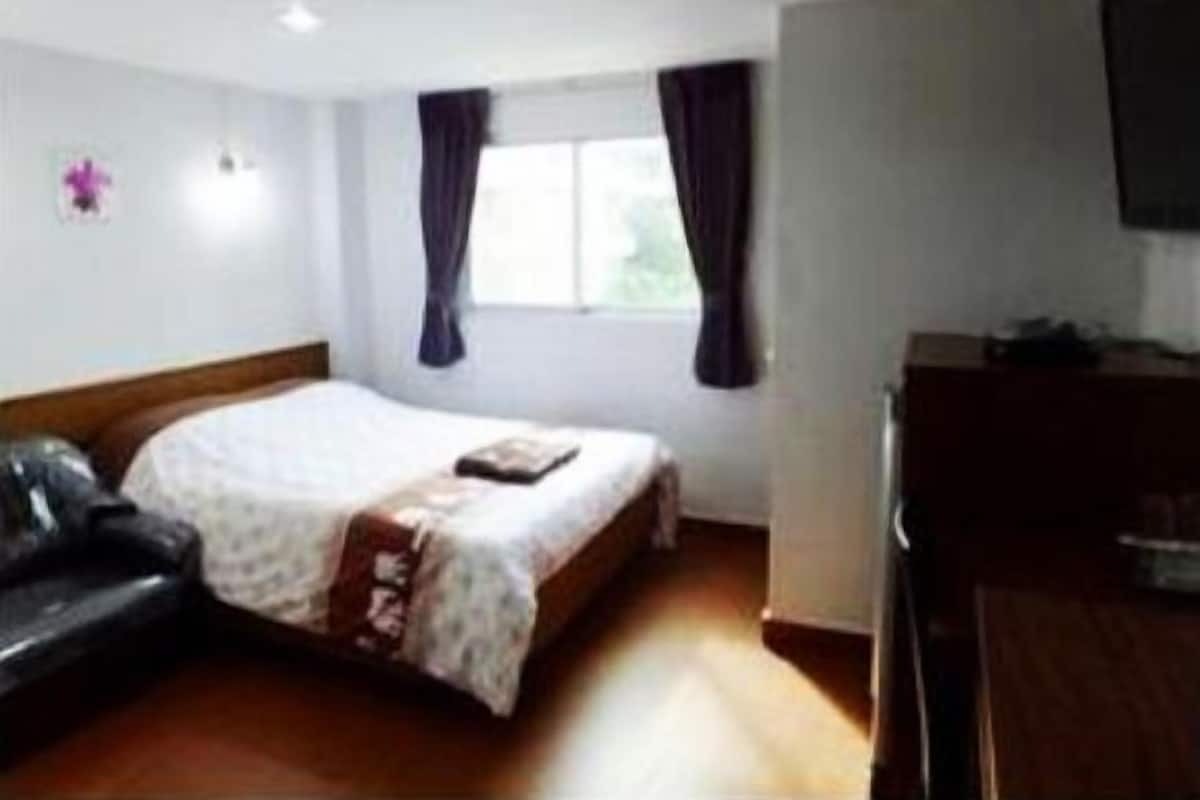 A hotel room with a bed, a desk, a chair, and a window with curtains.