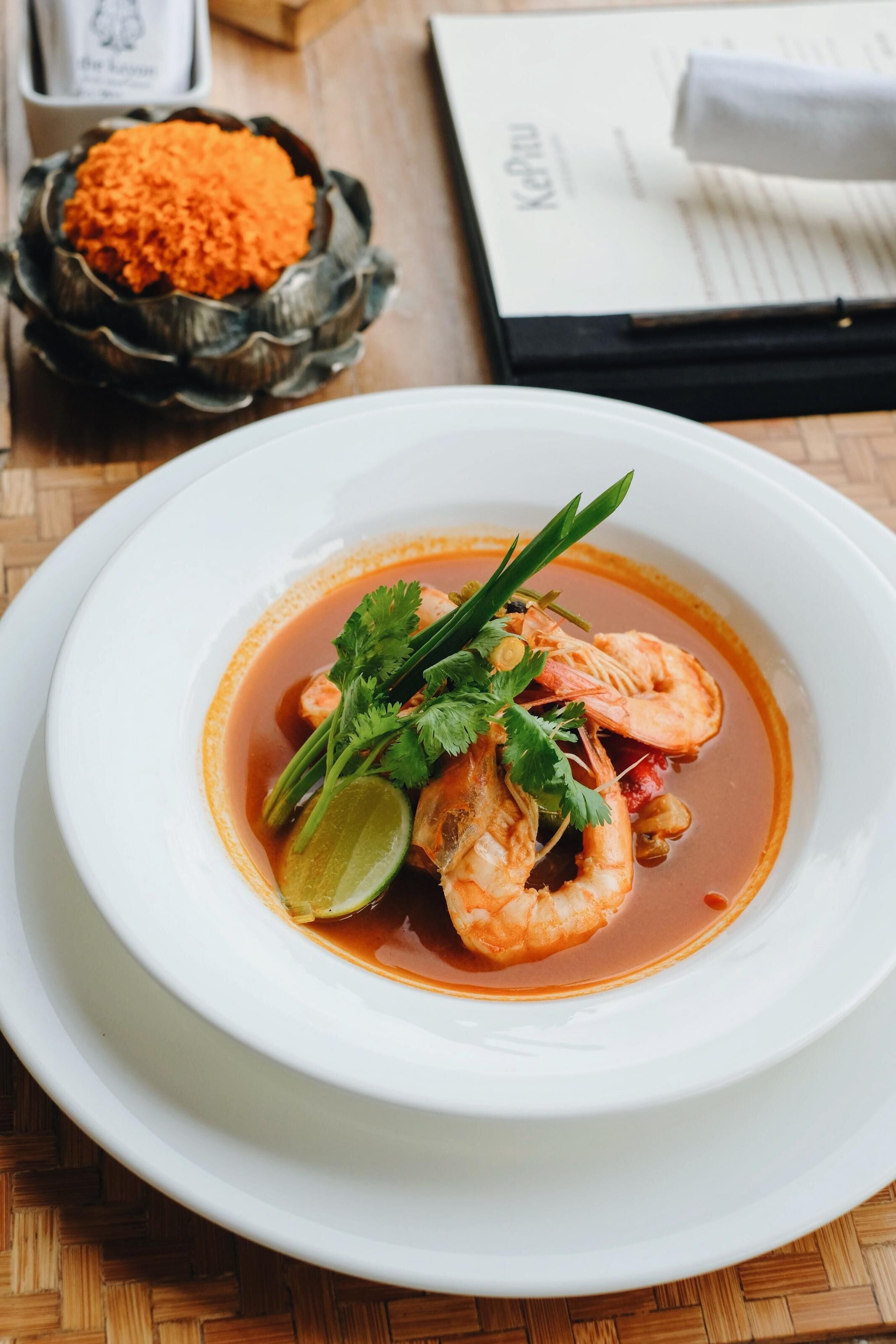 A white plate with a seafood dish, garnished with cilantro and lime, on a wooden table.