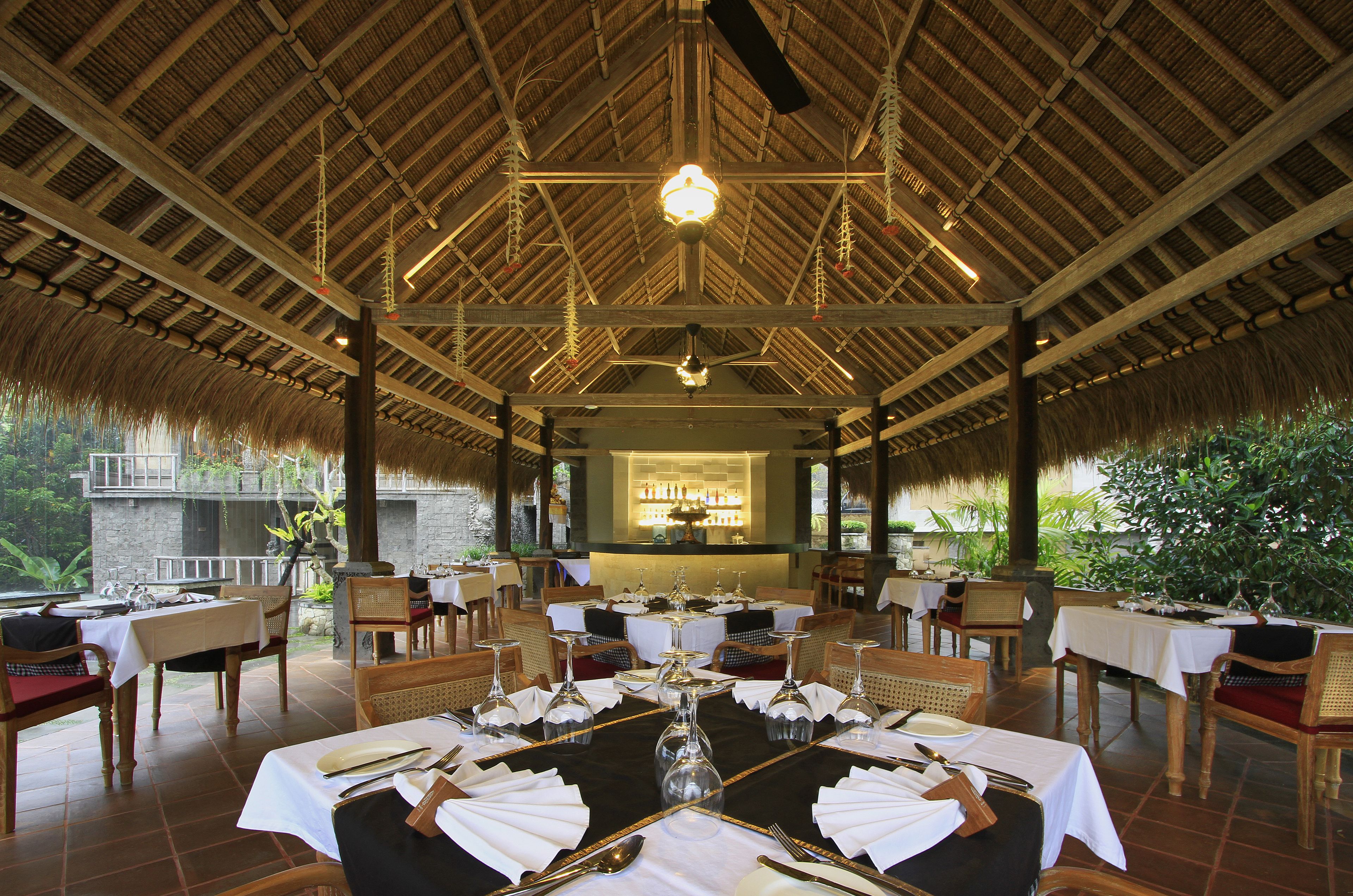 A restaurant with thatched roof, wooden tables, and chairs set for dining.