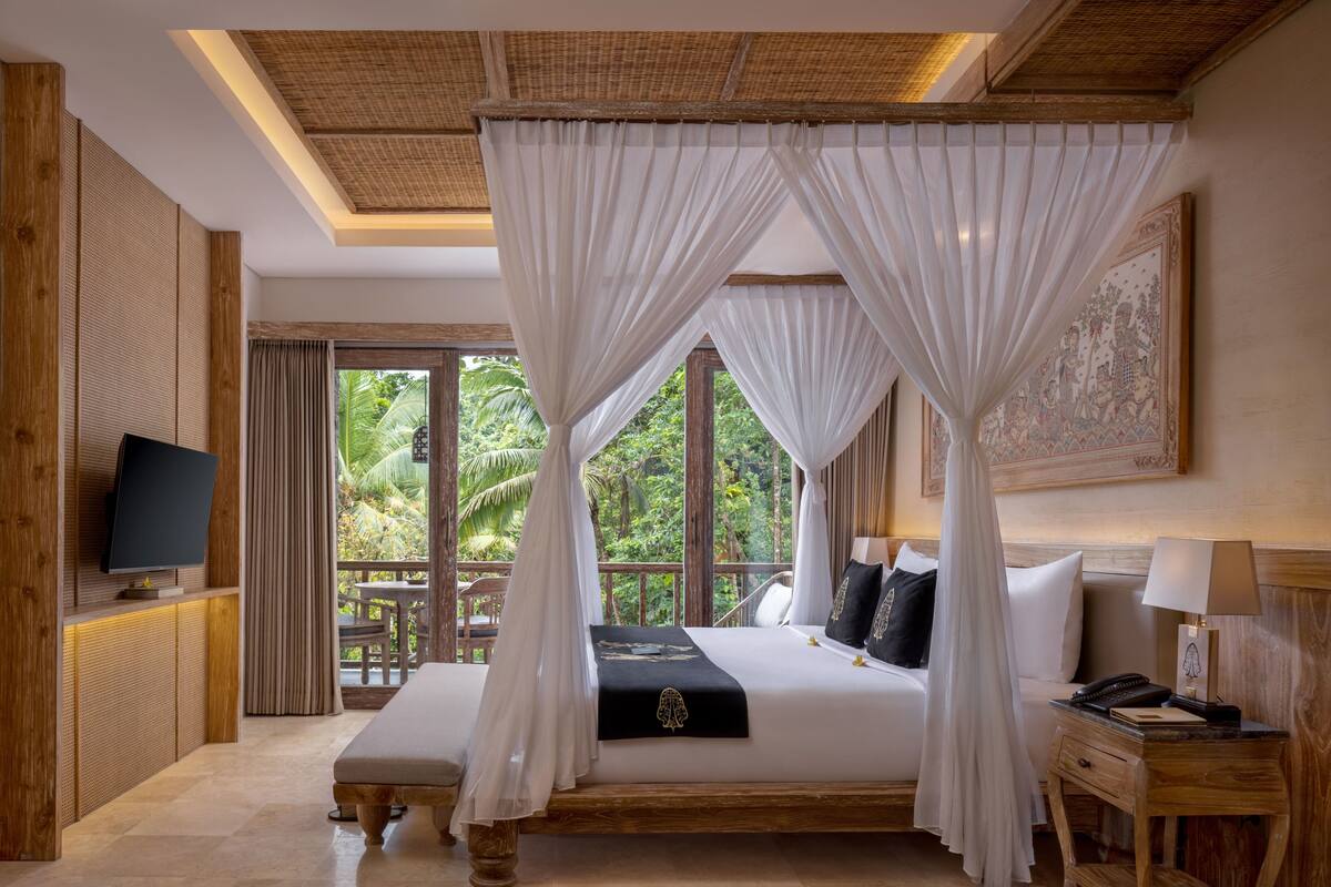 Ein Schlafzimmer mit Himmelbett, Fernseher, Nachttisch und Blick auf üppiges Grün.