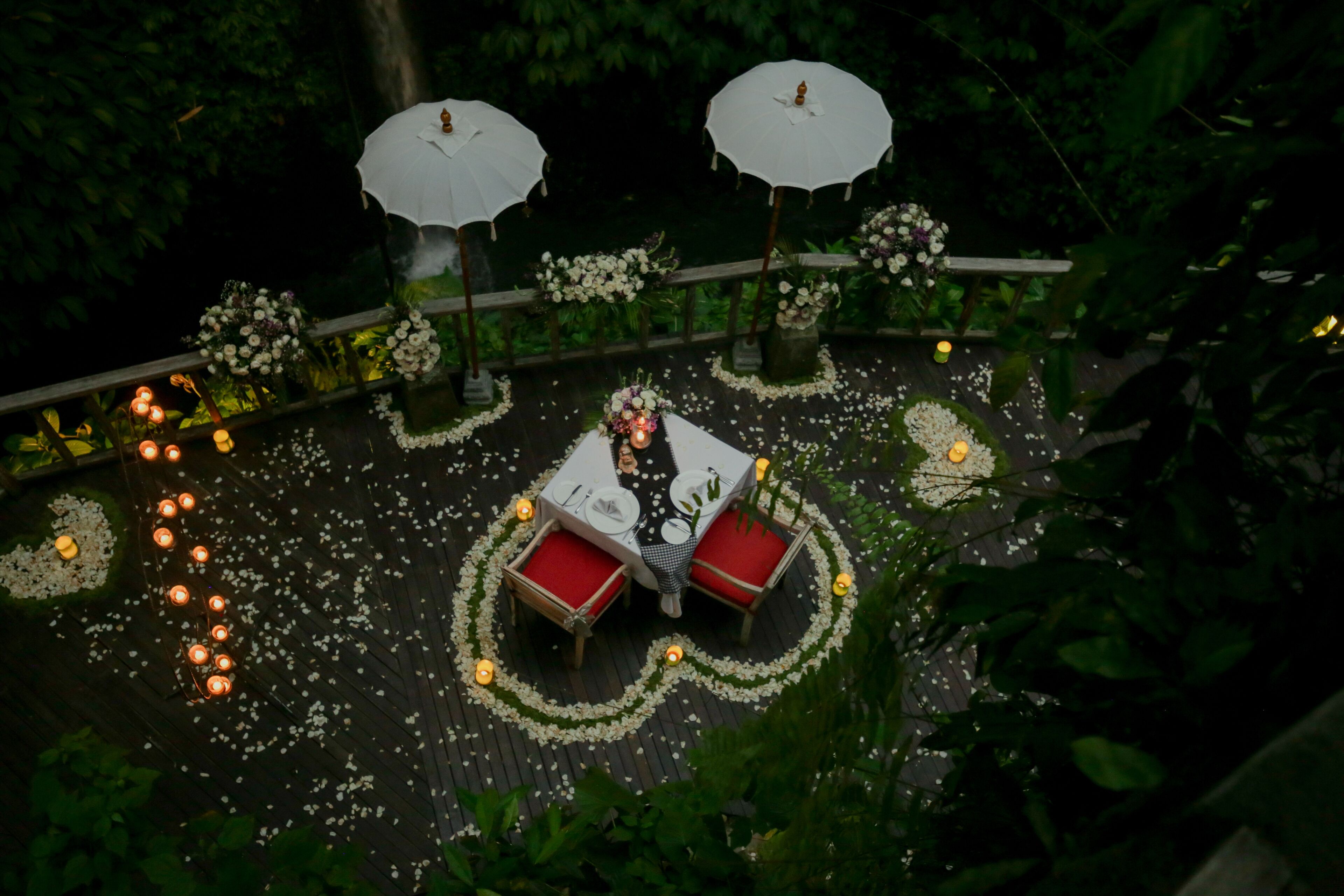 An outdoor dining area with tables and chairs, surrounded by flower petals and candles.