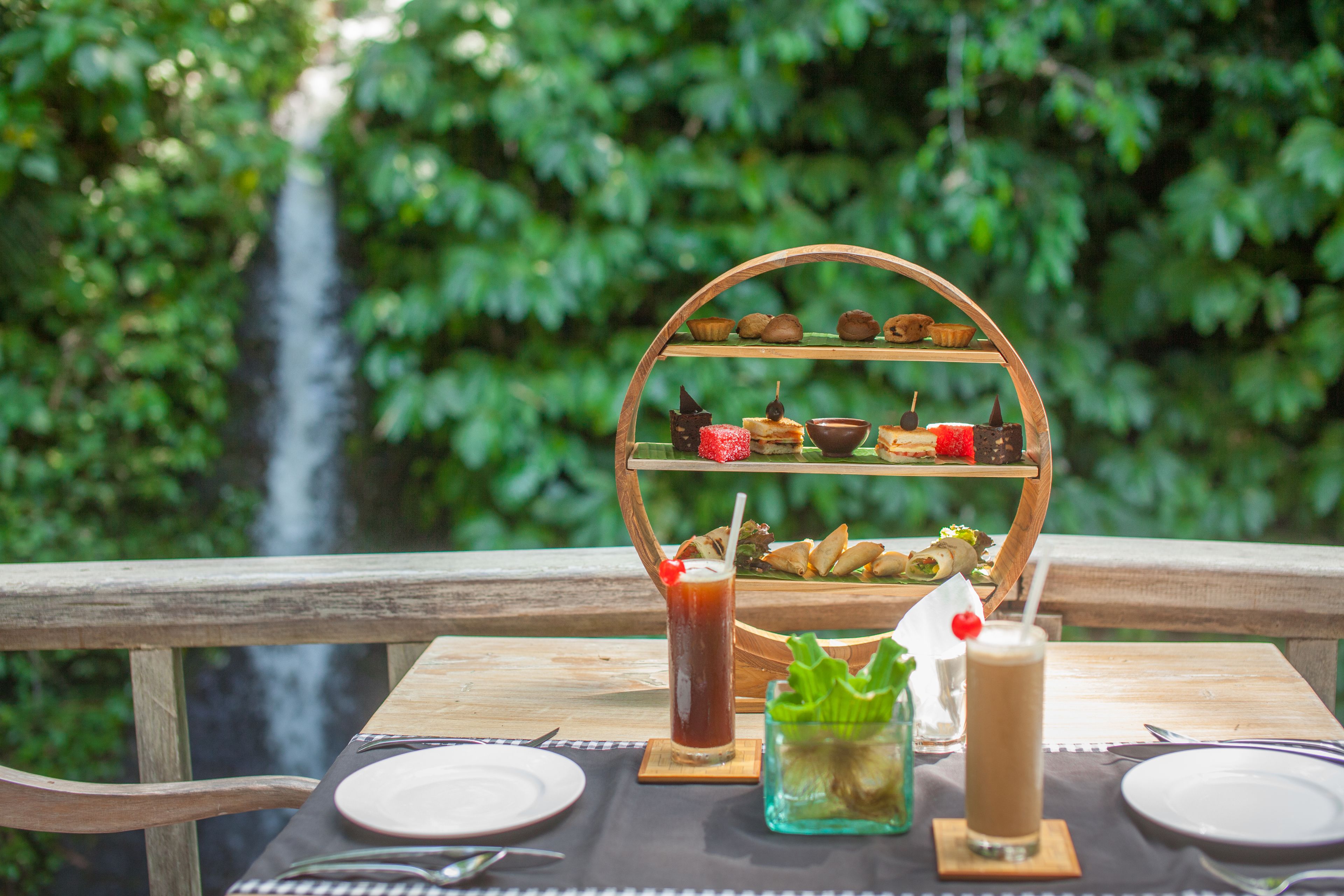 A table set with plates, cutlery, and a tiered dessert stand with various sweets and a drink.